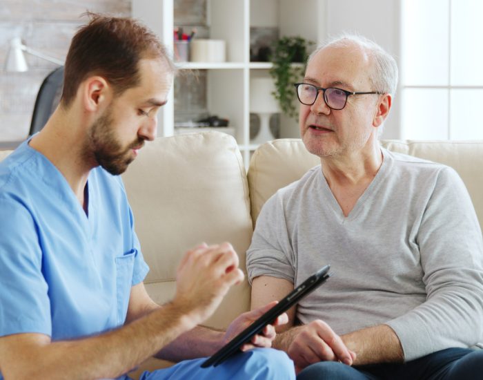 caucasian-male-nurse-talking-with-nursing-home-patient-about-his-health-nurse-is-making-notes-digital-tablet